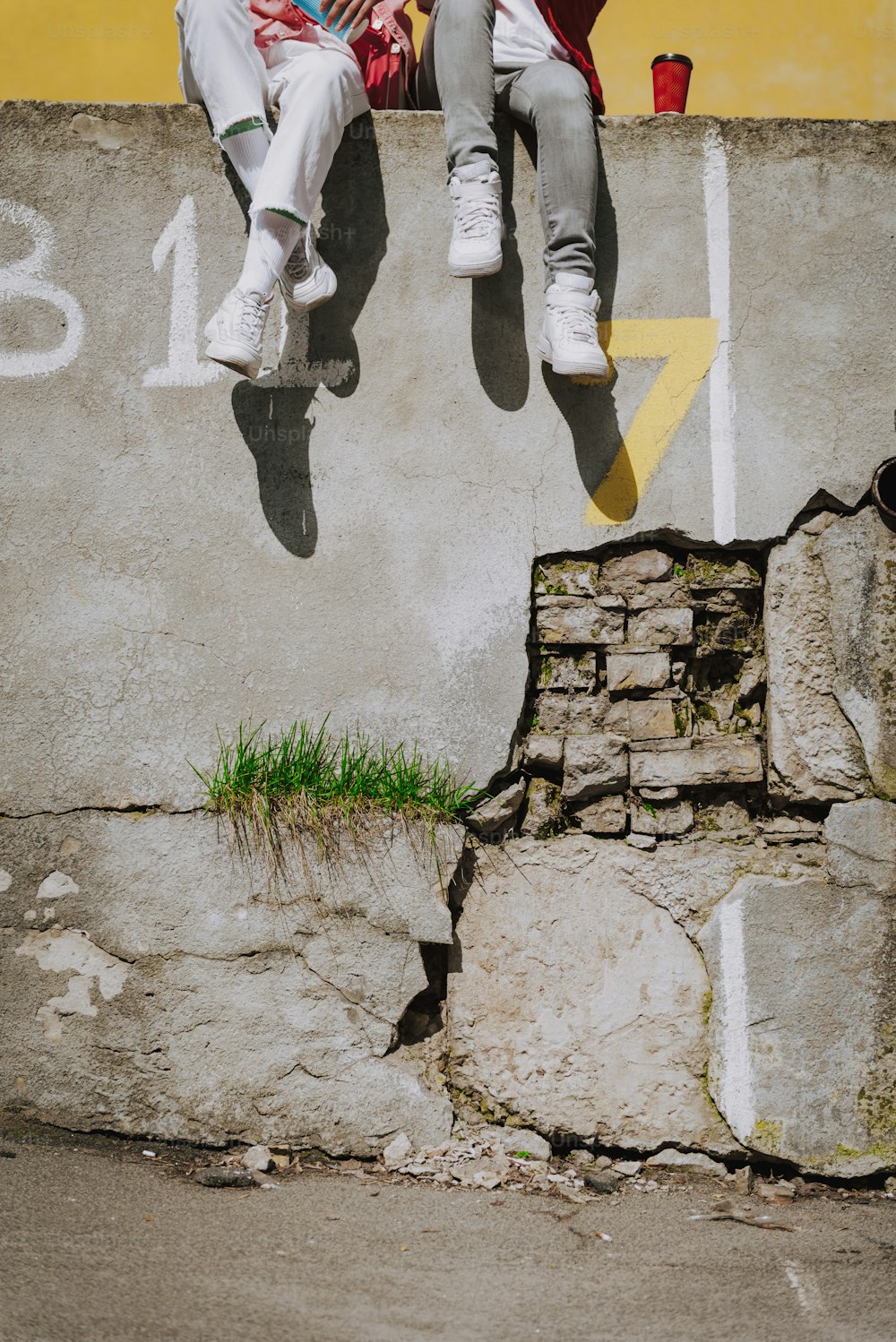 Urban lifestyle concept. Waist down portrait of two hipster ladies in sporty stylish clothes resting together on old parapet with coffee