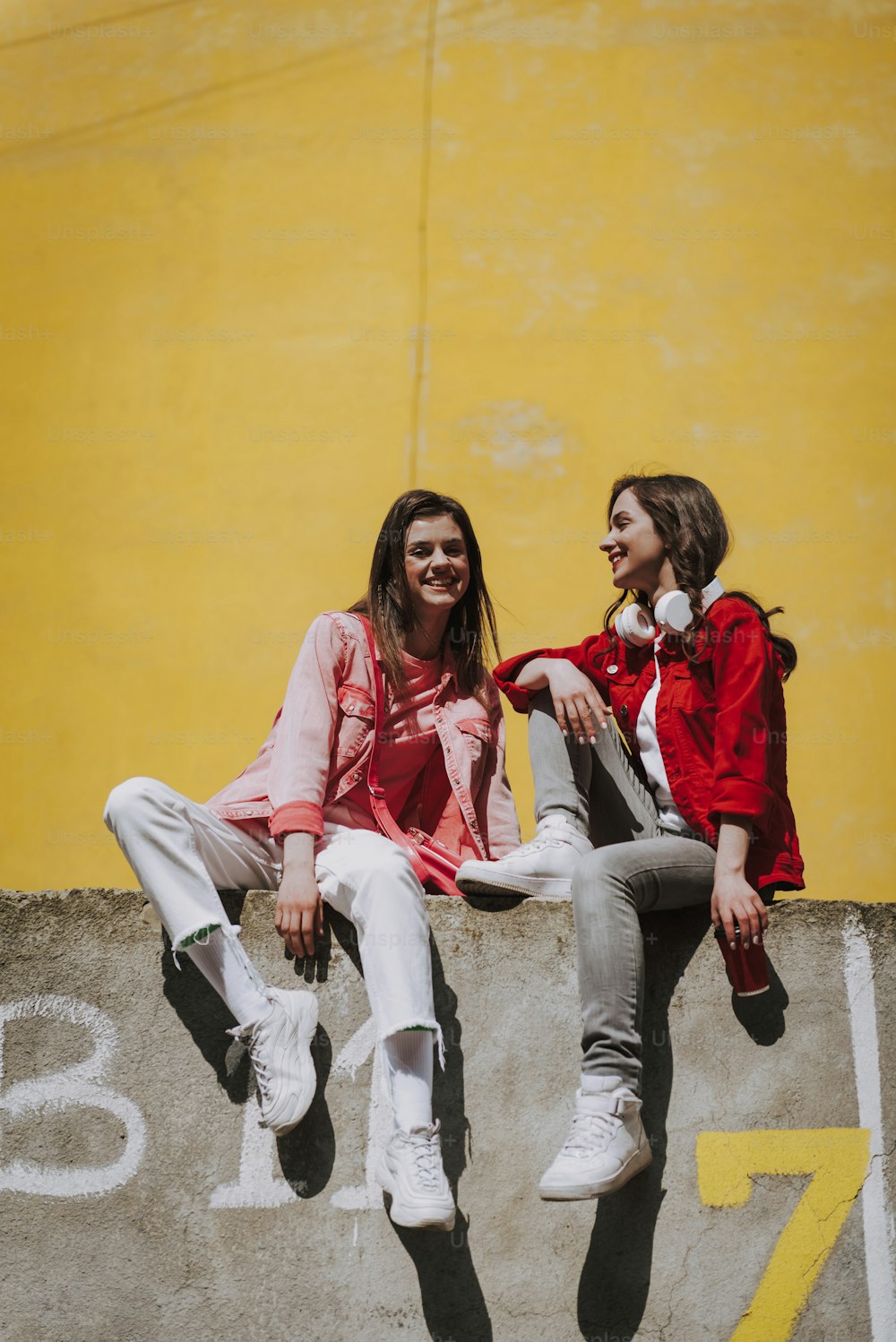 도시 생활 개념. 난간 벽에 함께 쉬고 있는 두 젊고 행복한 웃는 힙스터 여성의 전신 초상화