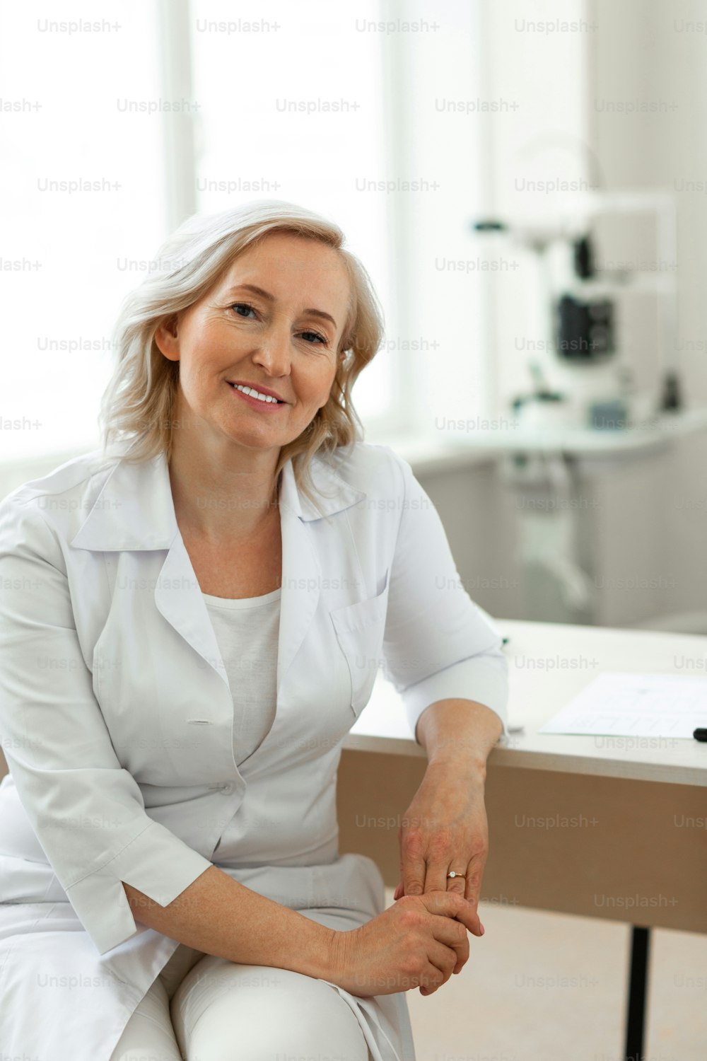 Intense working day . Short-haired doctor with light smile wearing white uniform while leaning on the table