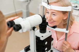 Head in metal frame. Senior good-looking woman visiting ophthalmologist and checking her eyesight with big device