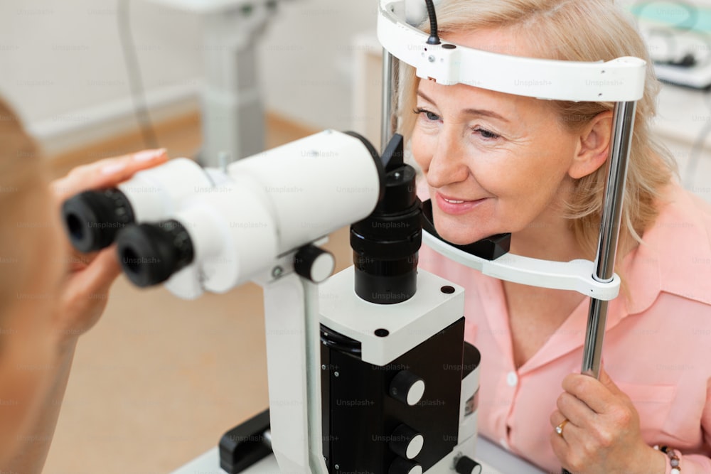金属フレームのヘッド。眼科医を訪ね、大きな装置で視力をチェックする年配の見栄えの良い女性
