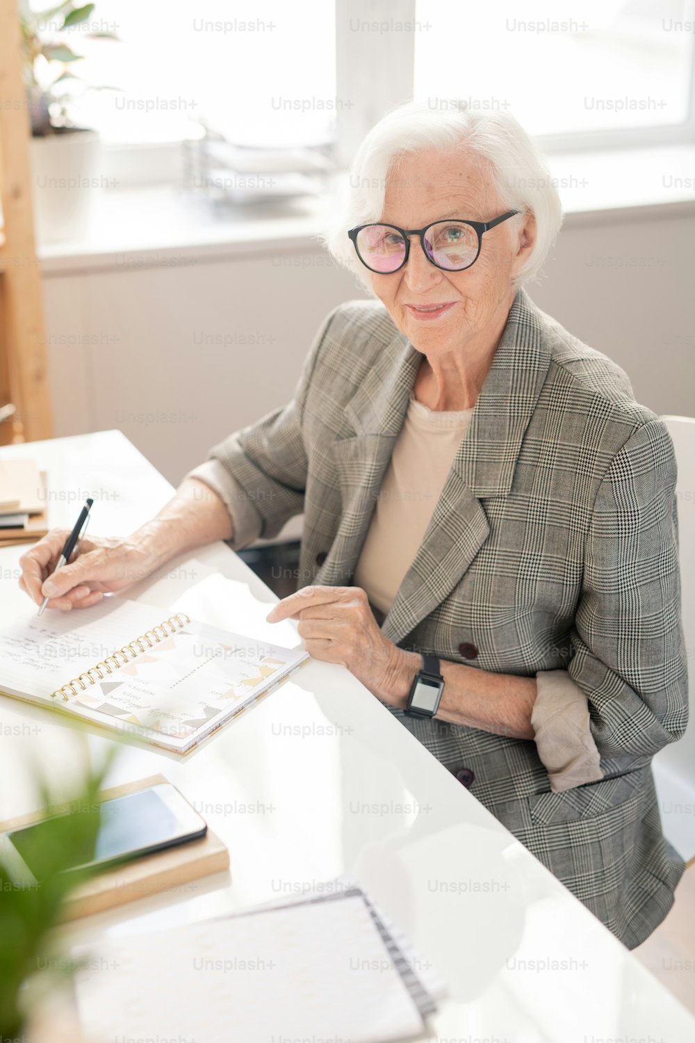 Trabalhador de escritório idoso bem-sucedido com cabelos brancos sentado ao lado da mesa enquanto planeja o dia de trabalho pela manhã