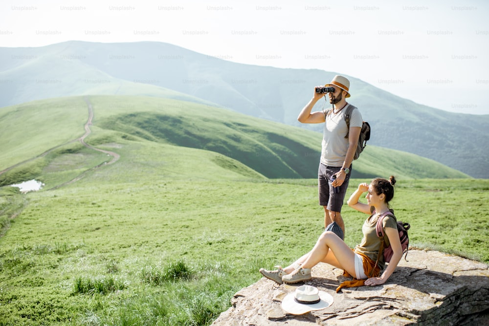 Couple enjoying beautiful landscape views, resting on the rock while traveling in the mountains during the summer time