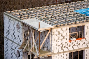 Edificio en construcción. Marco de vigas de techo y base de techo, barrera impermeable resistente al agua en paredes de bloques de aislamiento de espuma hueca. Albañilería, techado y renovación.