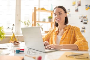 Jeune designer brun heureux ou étudiant regardant l’écran d’un ordinateur portable tout en surfant sur le net ou en recherchant des informations