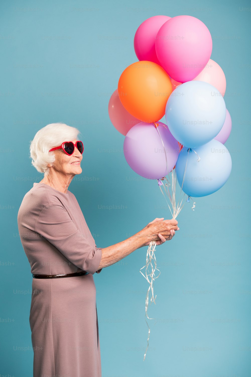 Elegante und liebenswürdige ältere Frau, die einen Haufen bunter Luftballons hält, während sie im Studio steht