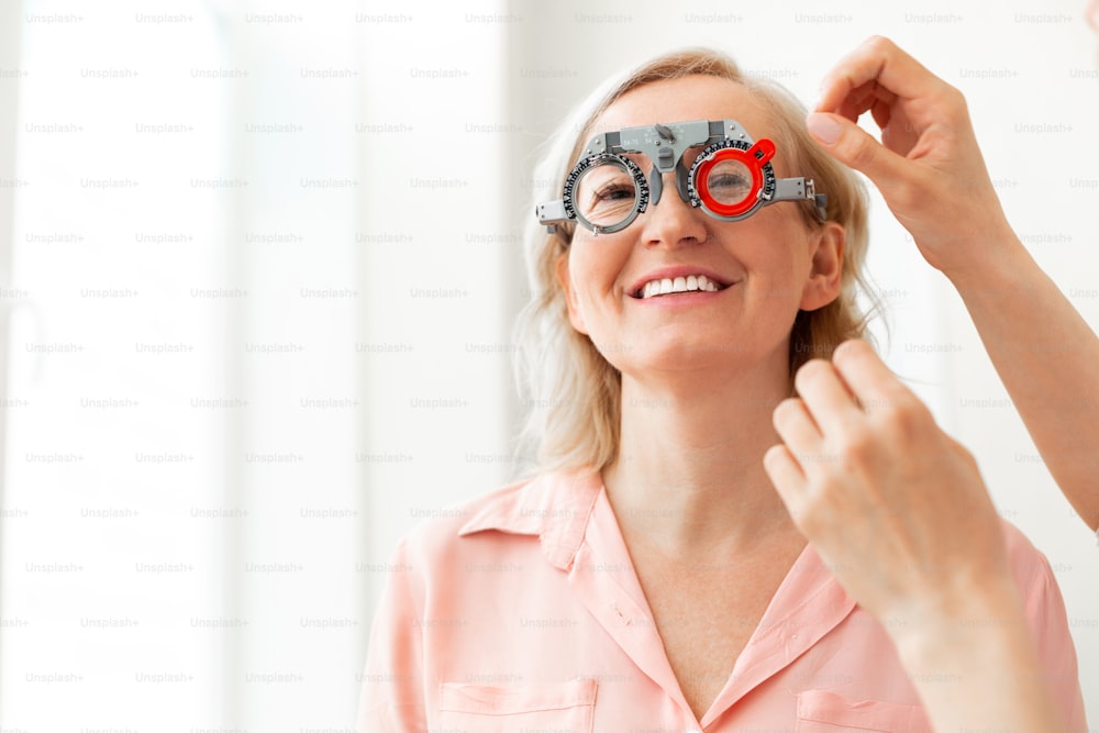 Tamanho da lente. Paciente de cabelos curtos com sorriso largo experimentando lentes diferentes enquanto tem consulta com oftalmologista