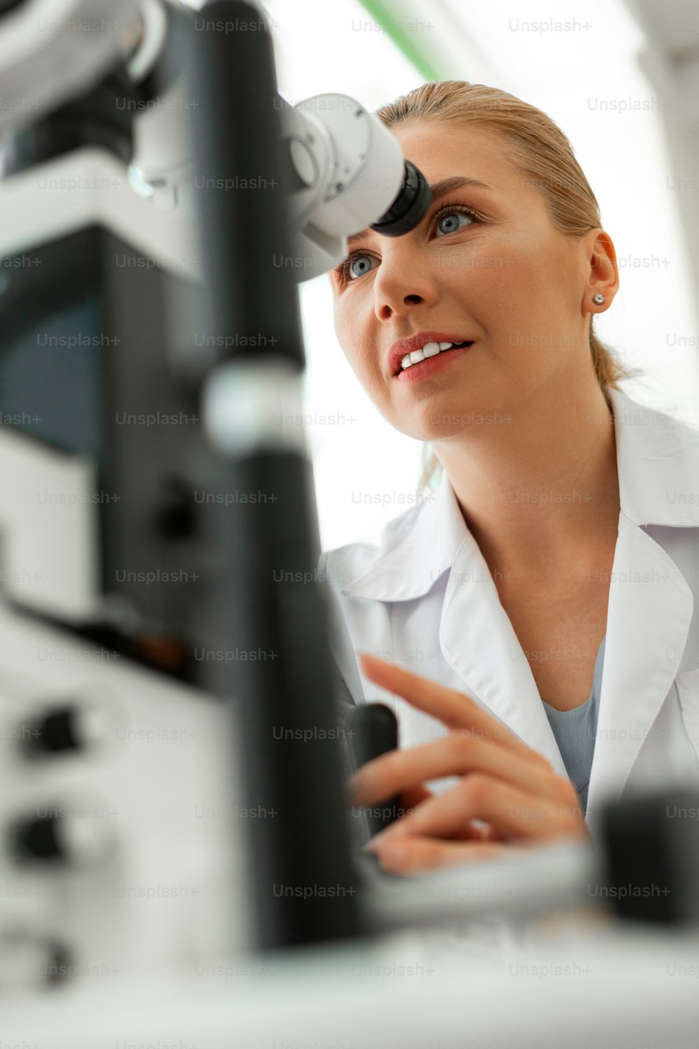 Sessões intensas. Médico sorridente agradável sendo concentrado em fotos no dispositivo enquanto olha no binóculo