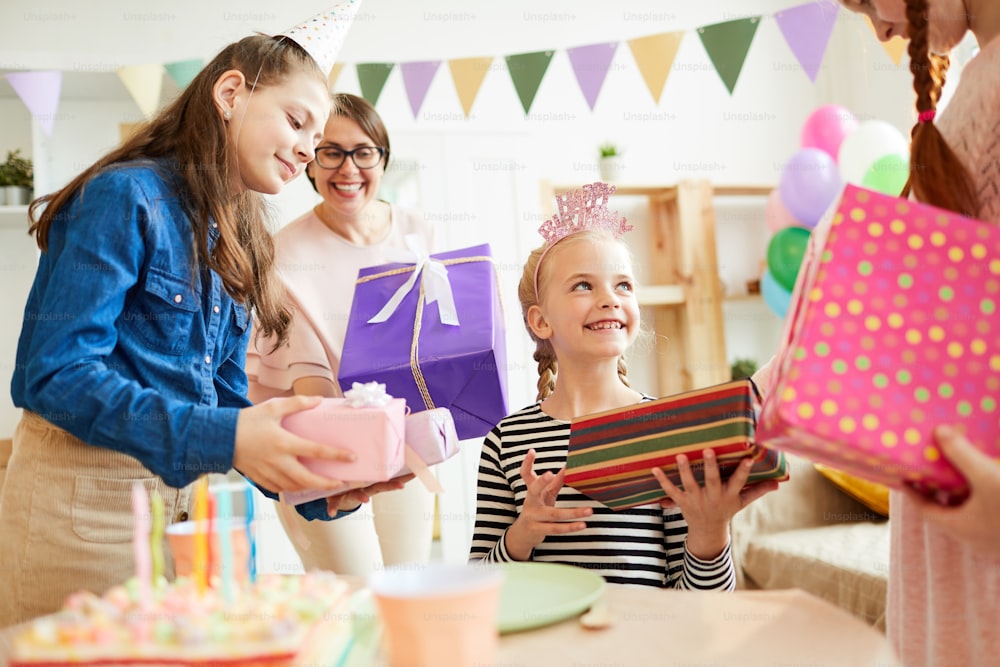 Portrait of cute girl receiving gifts surrounded by friends a during Birthday party, copy space