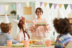 Portrait of happy mother bringing Birthday cake with candles for childrens party, copy space