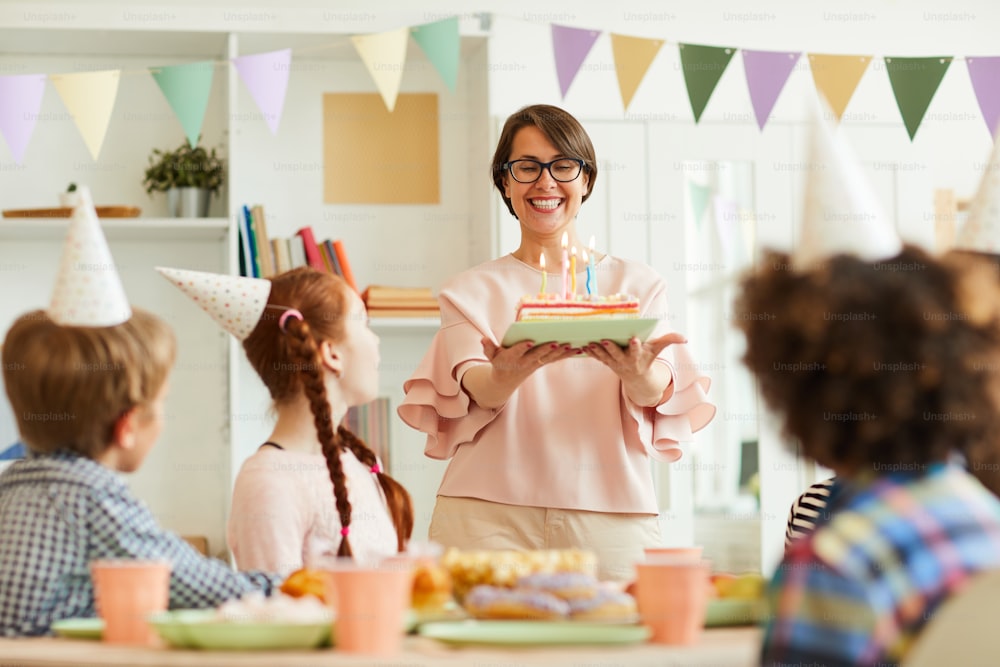 Portrait of happy mother bringing Birthday cake with candles for childrens party, copy space