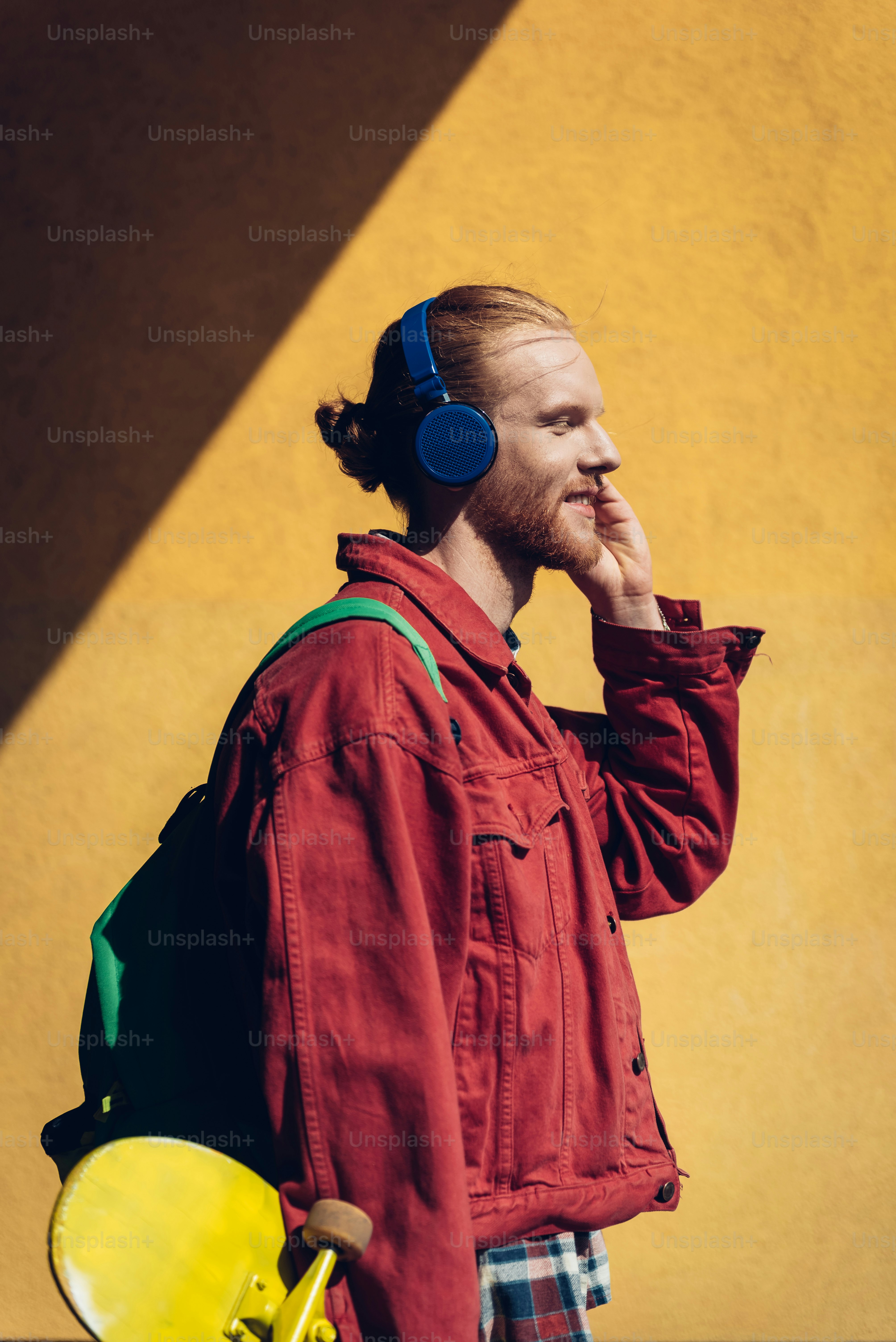 Gaya hidup dan aktivitas perkotaan. Pinggang di atas potret pria hipster muda yang tersenyum dengan skateboard kuning mendengarkan musik melalui headphone saat berjalan