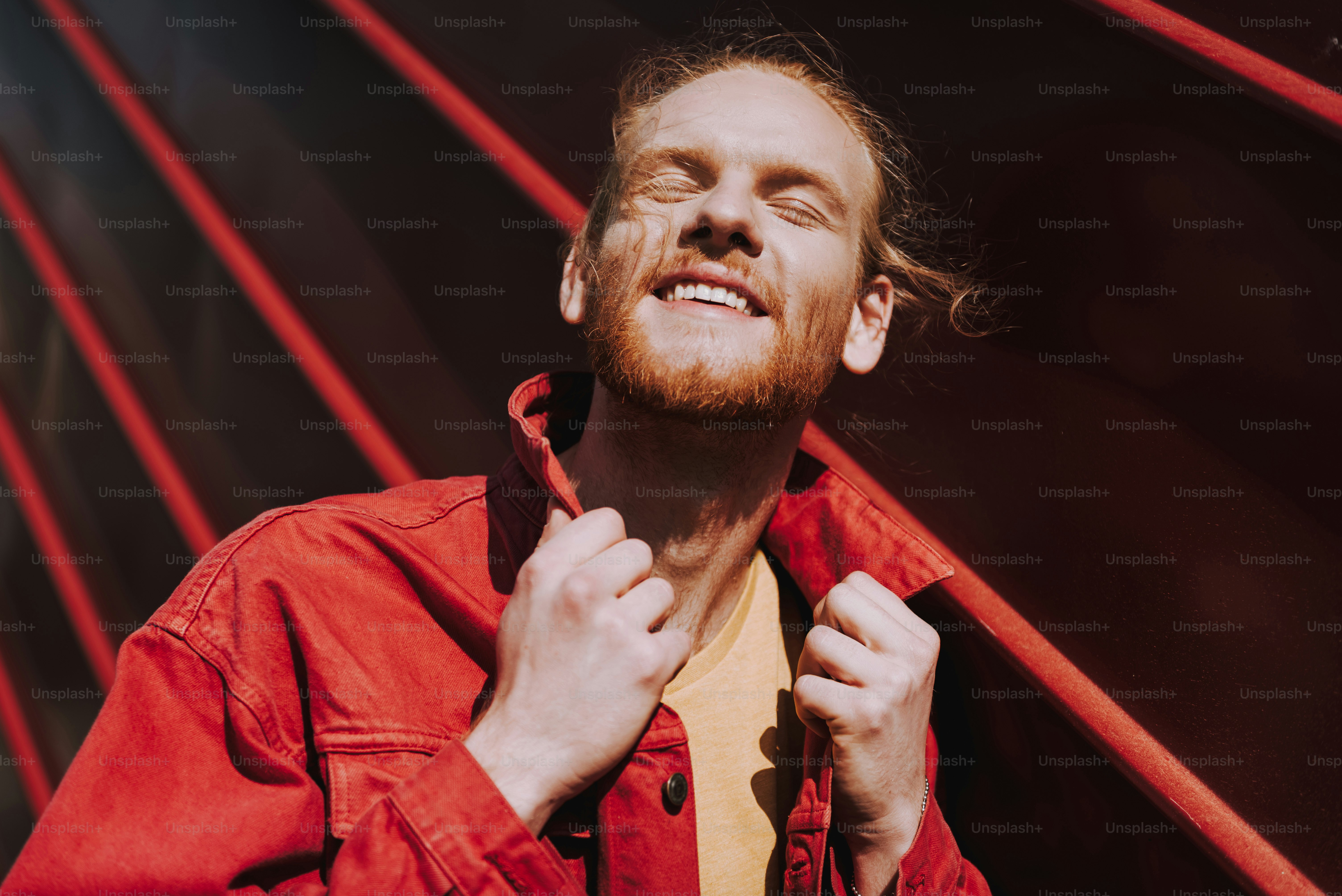 Urban lifestyle concept. Close up low angle portrait of smiling red haired hipster guy closing eyes enjoying sun shine on city view