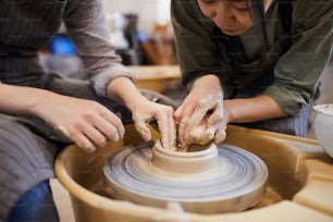 ワークショップでろくろを使って粘土皿を成形する方法を女性に示す熟練したアジアの女性陶芸家の接写