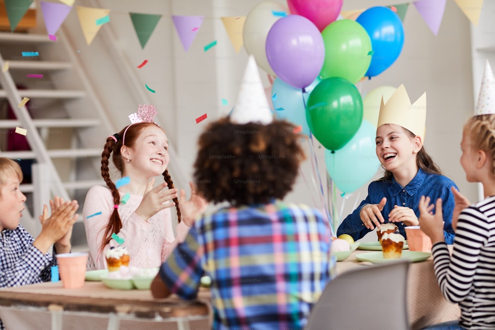 Grupo de crianças felizes se divertindo durante a festa de aniversário em sala decorada com confetes, espaço de cópia