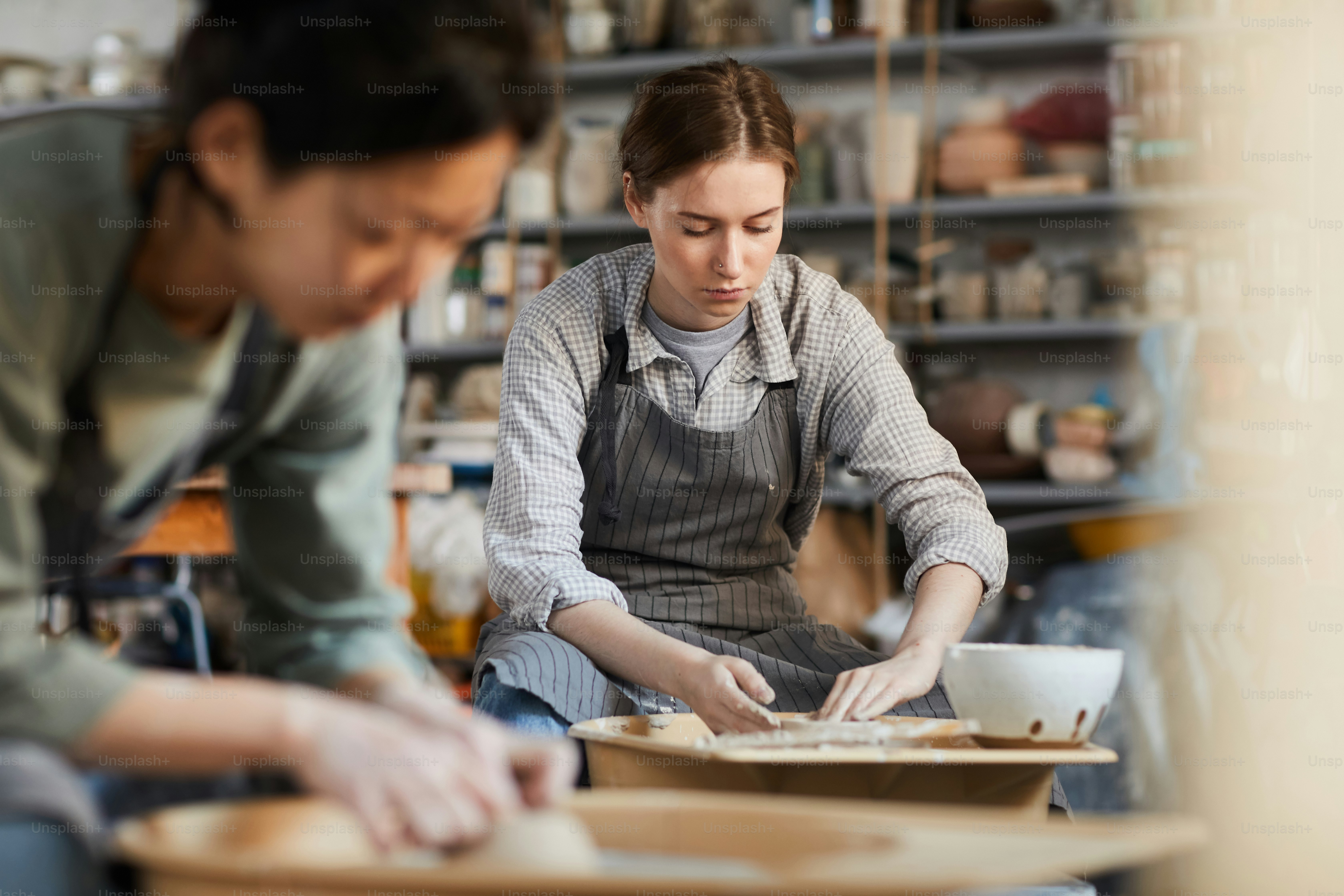 Close-up of concentrated Asian craftswoman in apron sitting at pottery ...