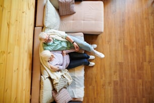 Überblick über einen erholsamen älteren Mann und eine Frau in Freizeitkleidung, die auf der Couch vor dem Fernseher sitzen und sich in ihrem Landhaus entspannen