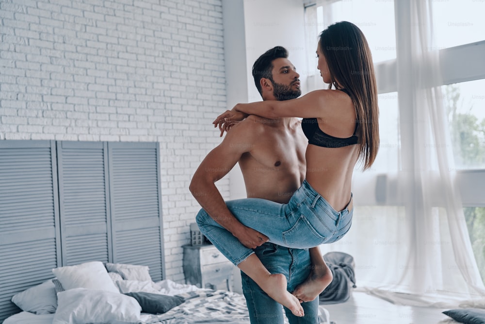 Beautiful young couple embracing while standing face to face in the bedroom