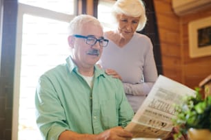 진지한 남자는 아침에 시골집 탁자 옆에 앉아 아내에게 신선한 소식을 읽어준다