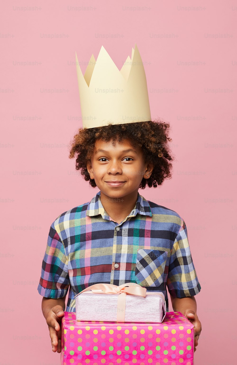 ピンクの背景にポーズをとるプレゼントを持つ笑顔のアフリカ系アメリカ人の少年のウエストアップポートレート、誕生日パーティーのコンセプト