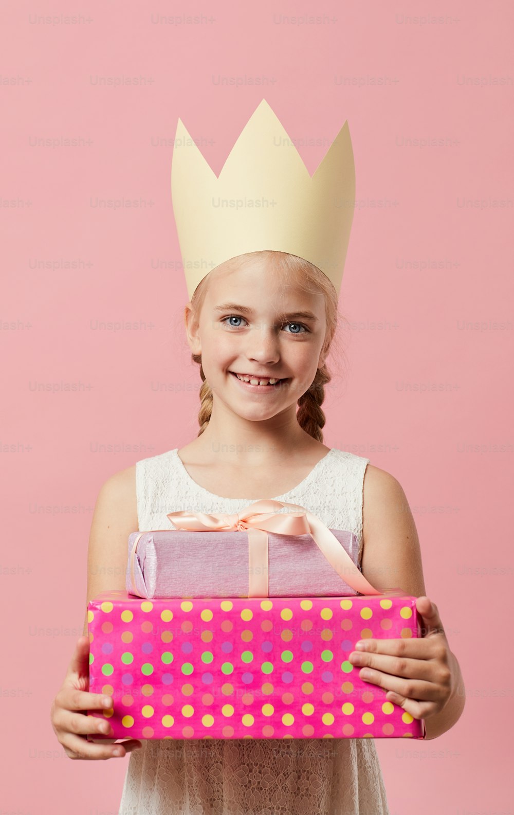 Retrato de cintura para arriba de una linda niña con corona posando contra fondo rosa, concepto de fiesta de cumpleaños