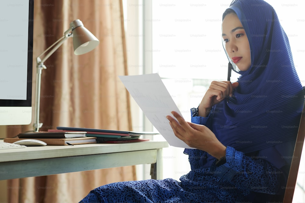 Joven vietnamita pensativa con hijab analizando el cuadro financiero en sus manos