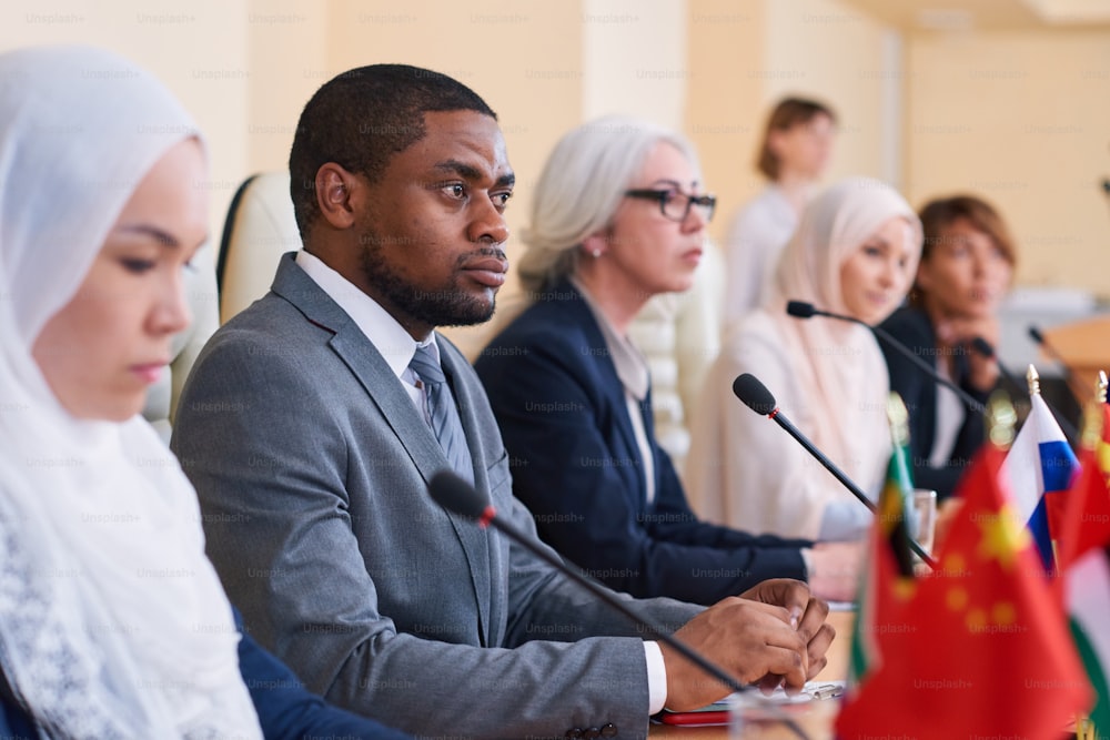 Young serious African-american businessman, participant of conference, listening attentively to one of speakers report