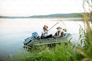 Nonno con figlio adulto che pesca sul gommone sul lago con canna verde in primo piano la mattina presto