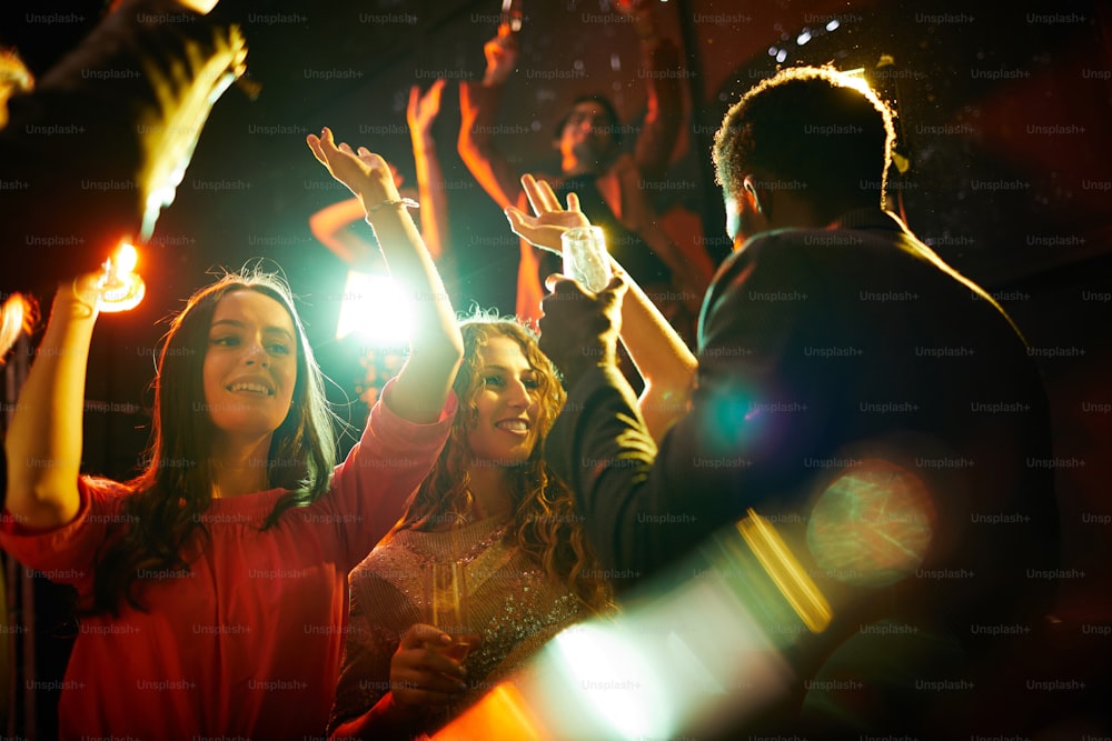 Chicas hermosas felices con blusas elegantes bebiendo champán y bailando en una fiesta en un club nocturno