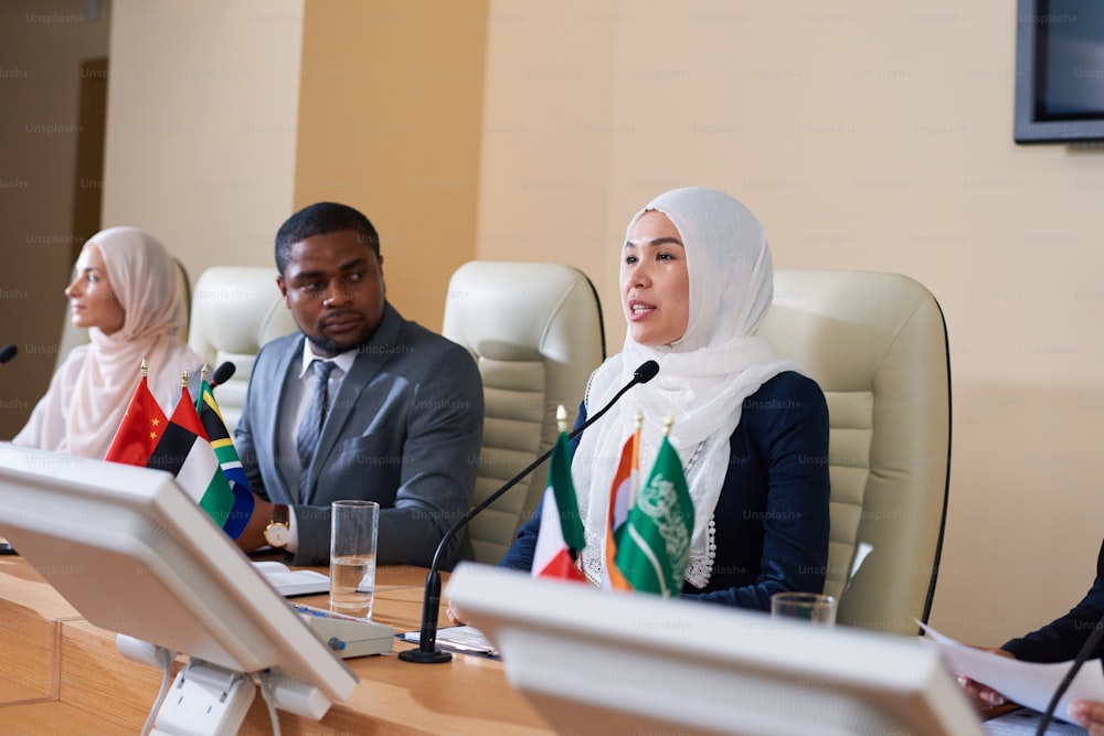 One of young female speakers in hijab talking in microphone while making speech in front of audience at business or political conference