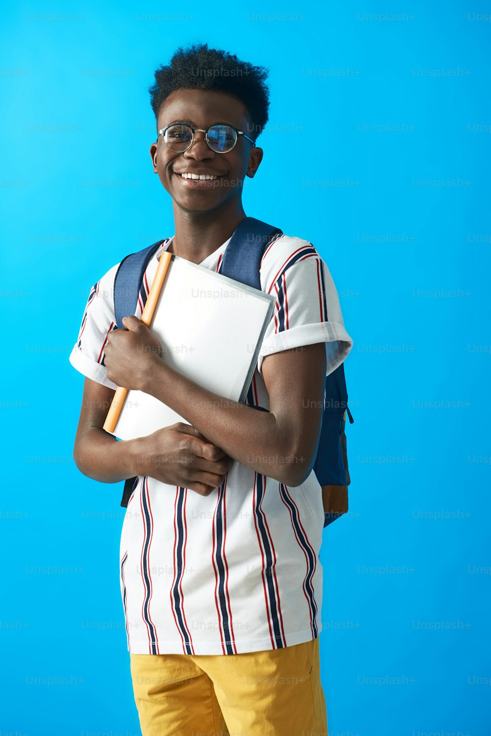 Waist up portrait of Aframerican young guy wearing striped t-shirt and holding files. Isolated on blue background