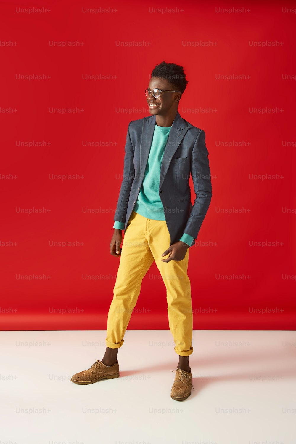 Retrato de corpo inteiro do jovem Aframerican em jaqueta e óculos. Ele está desviando o olhar e sorrindo