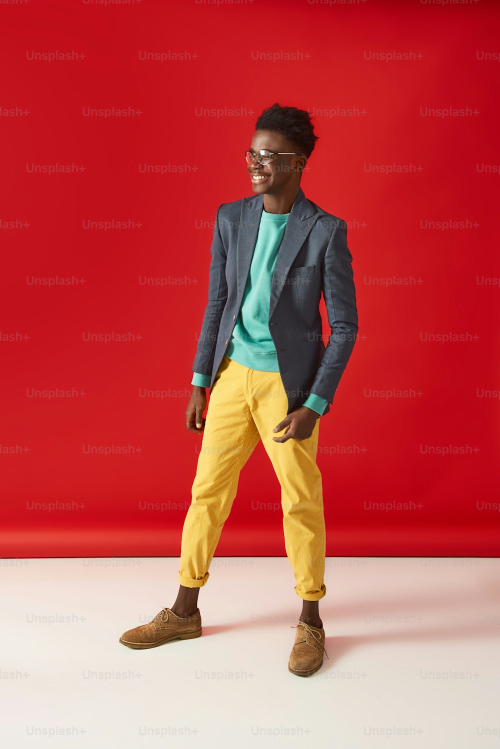 Ritratto a figura intera del giovane afroamericano in giacca e occhiali. Distoglie lo sguardo e sorride