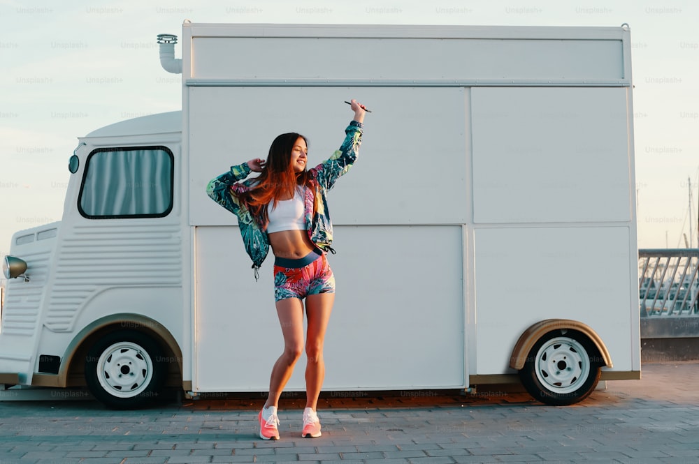 Full length of attractive young woman in sports clothing dancing while standing against food truck outdoors