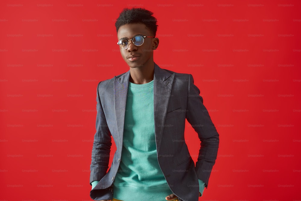 Ritratto in vita di ragazzo Aframerican in abiti eleganti che tengono le mani nelle tasche. Isolato su sfondo rosso