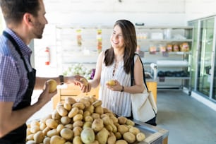 Smiling shopper getting some assistance from store owner in selecting potatoes at supermarket
