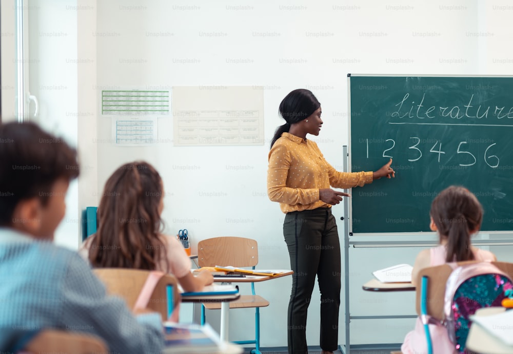 Professeur près du tableau noir. Professeur aux cheveux noirs portant un chemisier élégant debout près du tableau noir