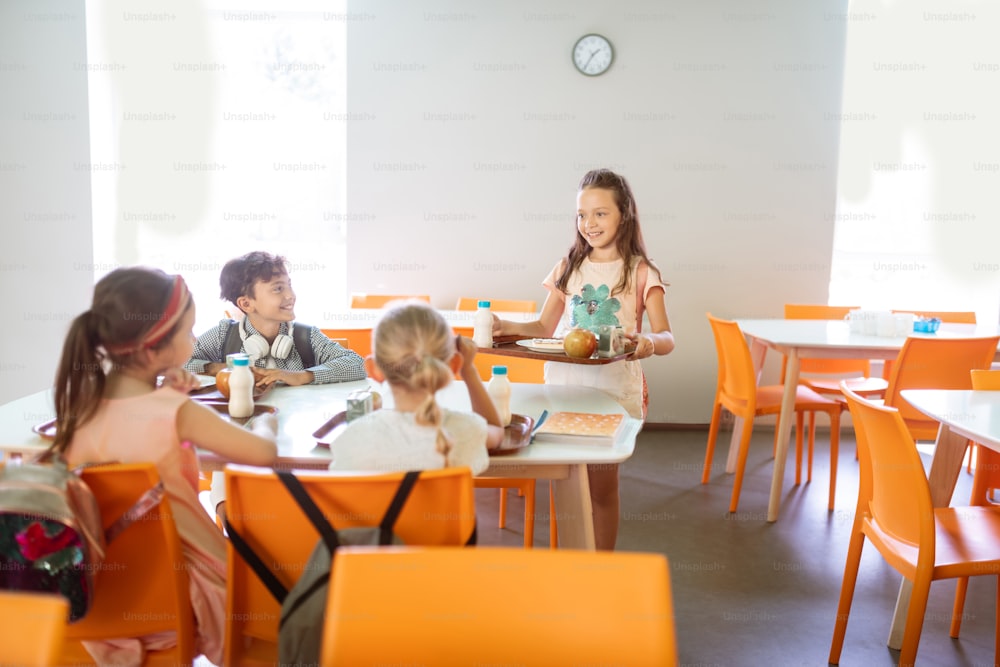 Lunch at school. Cute good-looking children feeling joyful while having lunch at school together