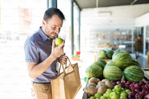 Homem cheirando maçã verde orgânica enquanto está em pé no supermercado