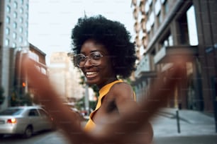 Waist up of smiling attractive lady in glasses walking on the street and looking at camera