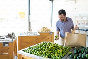 Mid adult man choosing fresh and healthy lemons while carrying shopping bag in store