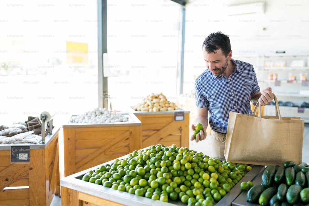 Mid adult man choosing fresh and healthy lemons while carrying shopping bag in store