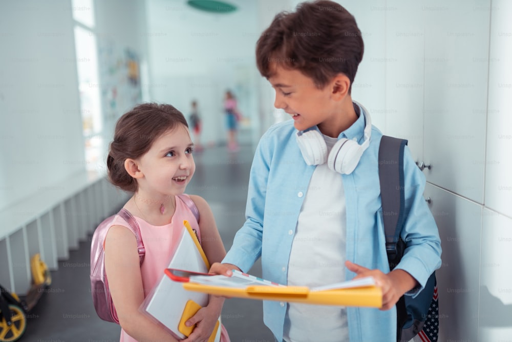 Falando com amigo. Estudante bonito usando fones de ouvido no pescoço falando com seu amigo na escola