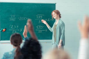 Ama il tuo lavoro. Insegnante gentile e sorridente che spiega le somme in piedi vicino alla lavagna in classe.