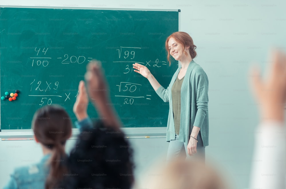 Ama il tuo lavoro. Insegnante gentile e sorridente che spiega le somme in piedi vicino alla lavagna in classe.