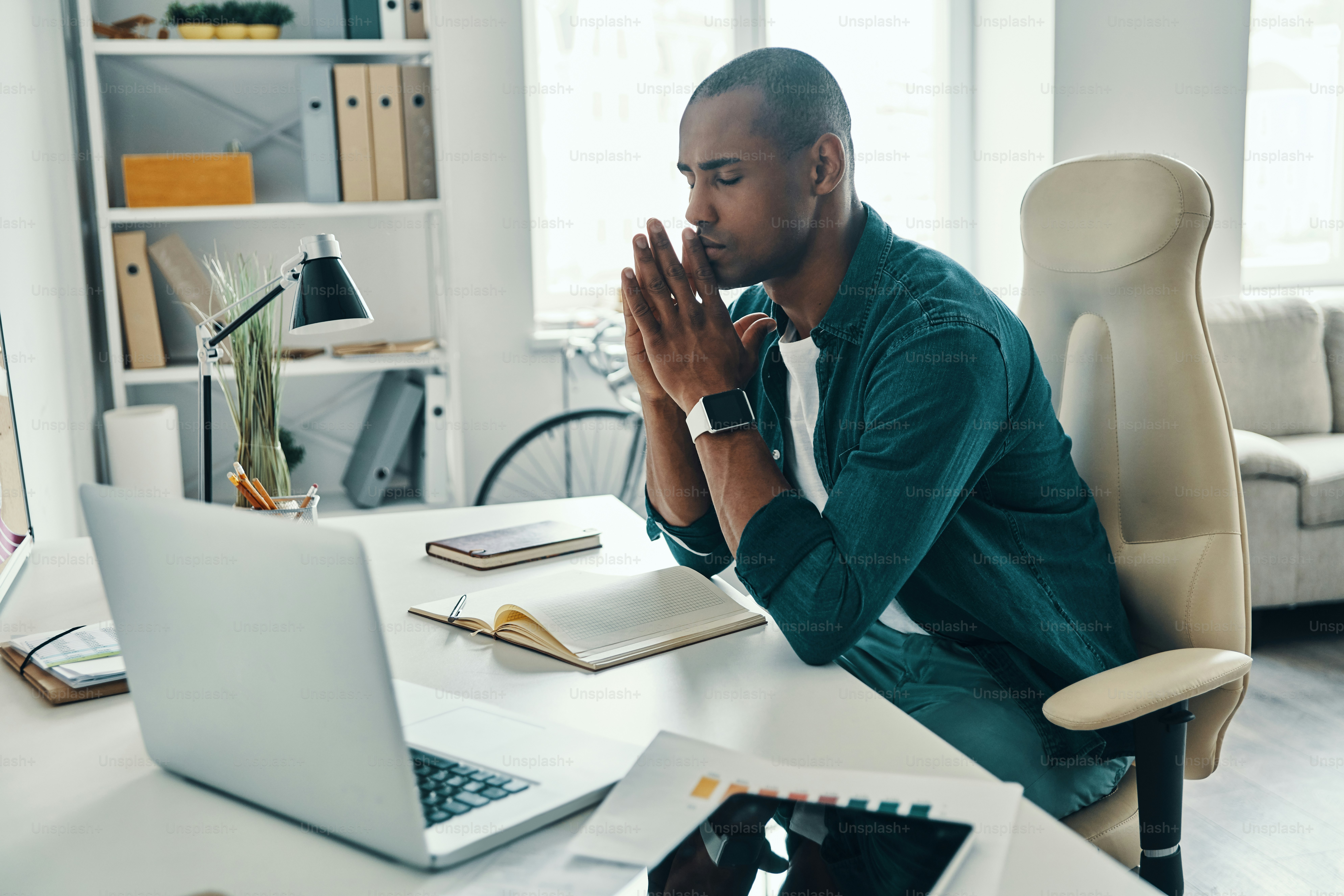 Tired young African man in shirt keeping eyes closed while sitting in the office