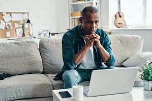 Handsome young African man using laptop while sitting indoors