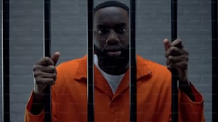 Prisionero negro sosteniendo rejas y mirando a la cámara, castigo de traficante de drogas