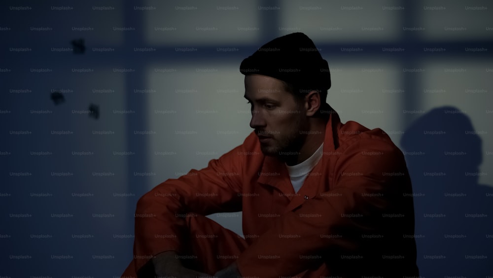 Depressiver Gefangener, der allein in einer dunklen Zelle sitzt und sich schuldig fühlt, weil er ein Verbrechen begangen hat