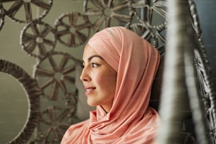 Hübsche lächelnde, nachdenkliche junge Frau mit Sommersprossen, die einen hellrosa Hijab trägt